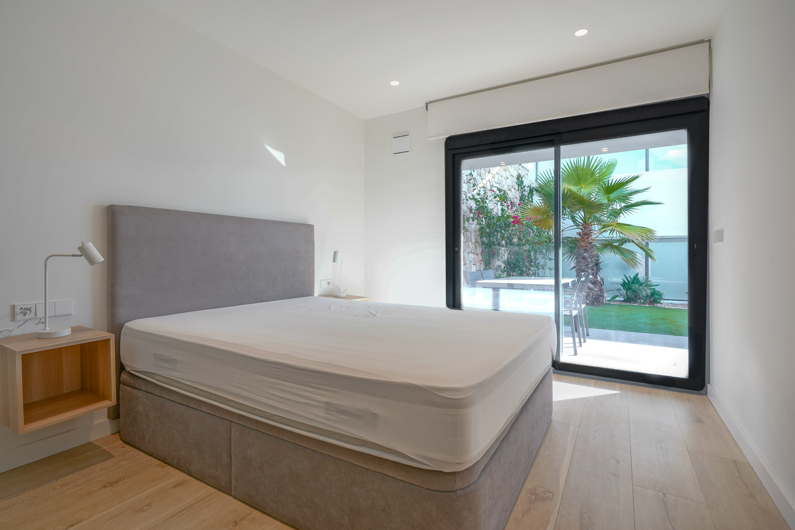 Chambre principale lumineuse avec accès direct au jardin, parquet en bois clair et grandes baies vitrées coulissantes offrant une vue sur la palmeraie.