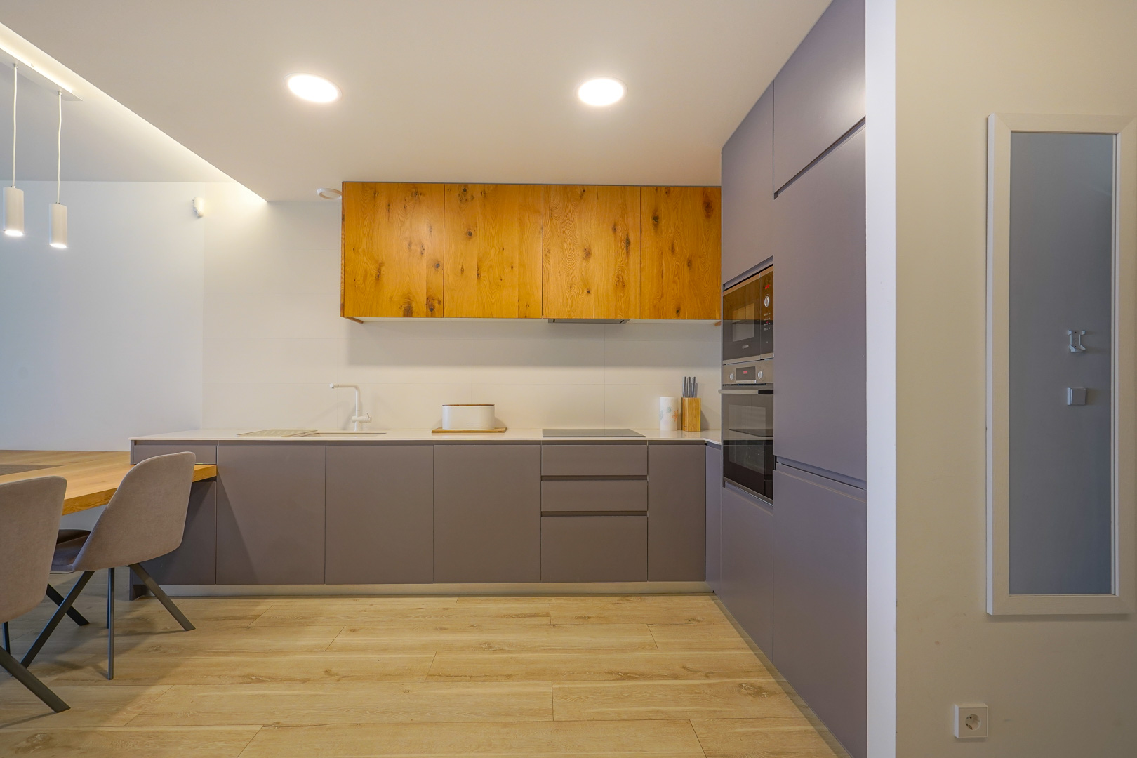 Cuisine moderne au design minimaliste avec des meubles gris mat et bois naturel, équipée d'appareils intégrés et d'un sol en grès cérame imitation bois.