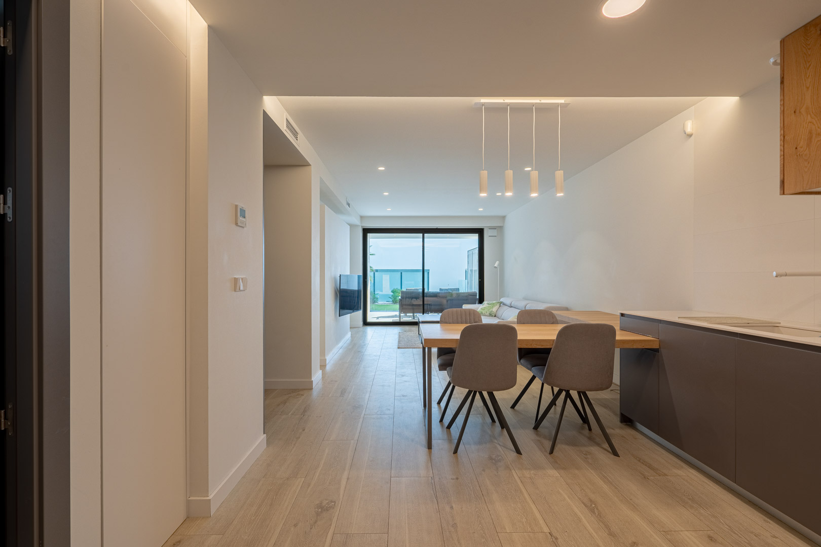 Espace de vie ouvert avec salle à manger, éclairage LED encastré, sols imitation bois et accès direct à la terrasse par de grandes baies vitrées.