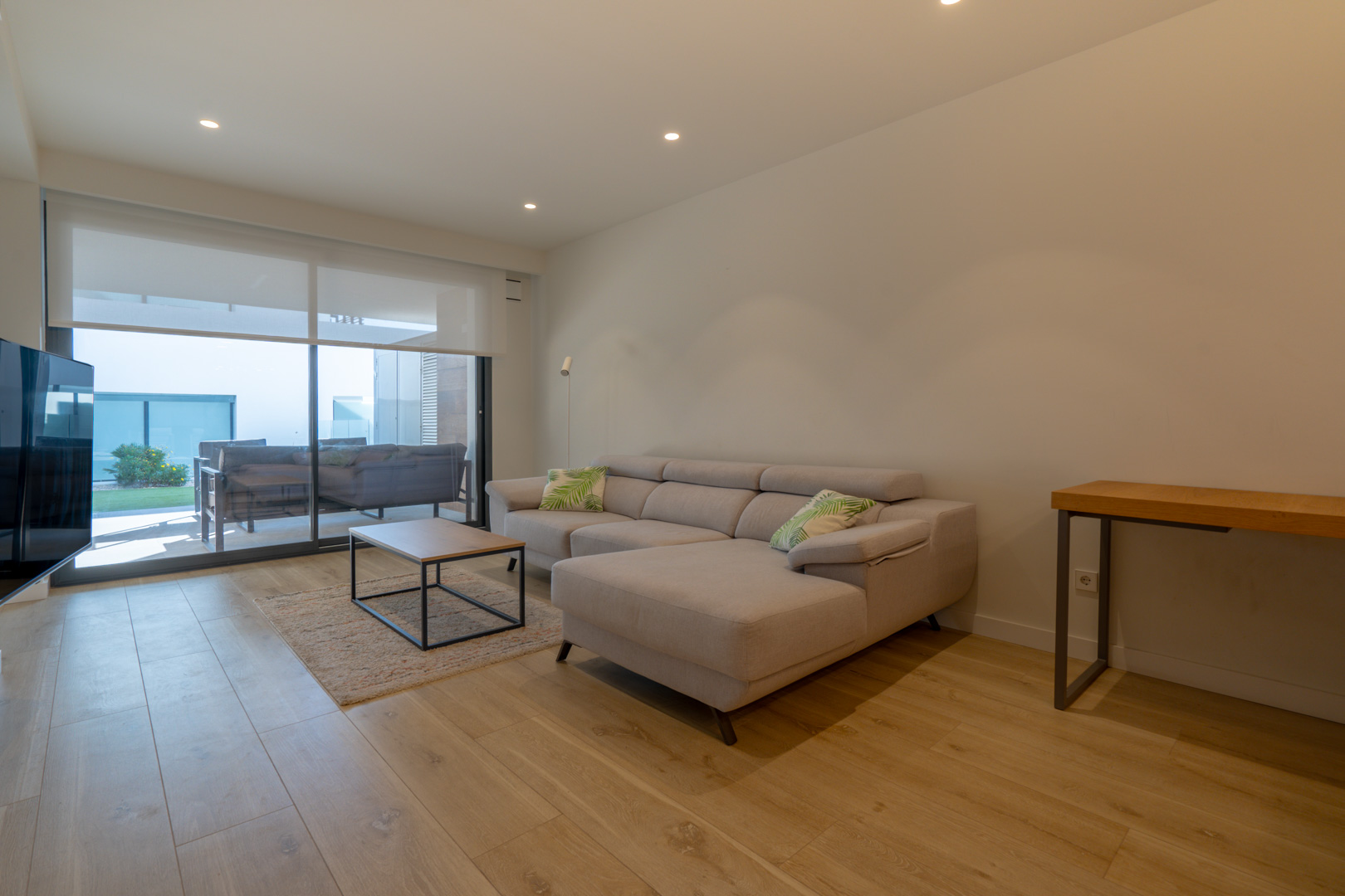 Salon contemporain avec canapé d'angle, parquet clair et grandes baies vitrées coulissantes offrant un accès direct à la terrasse couverte et au jardin.