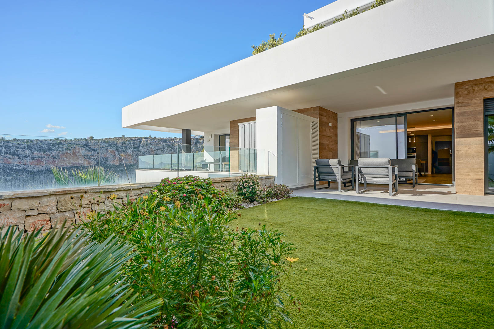 Terrasse couverte avec mobilier contemporain et jardin privé, bordée d'un mur en pierre naturelle offrant une vue dégagée sur le parc.