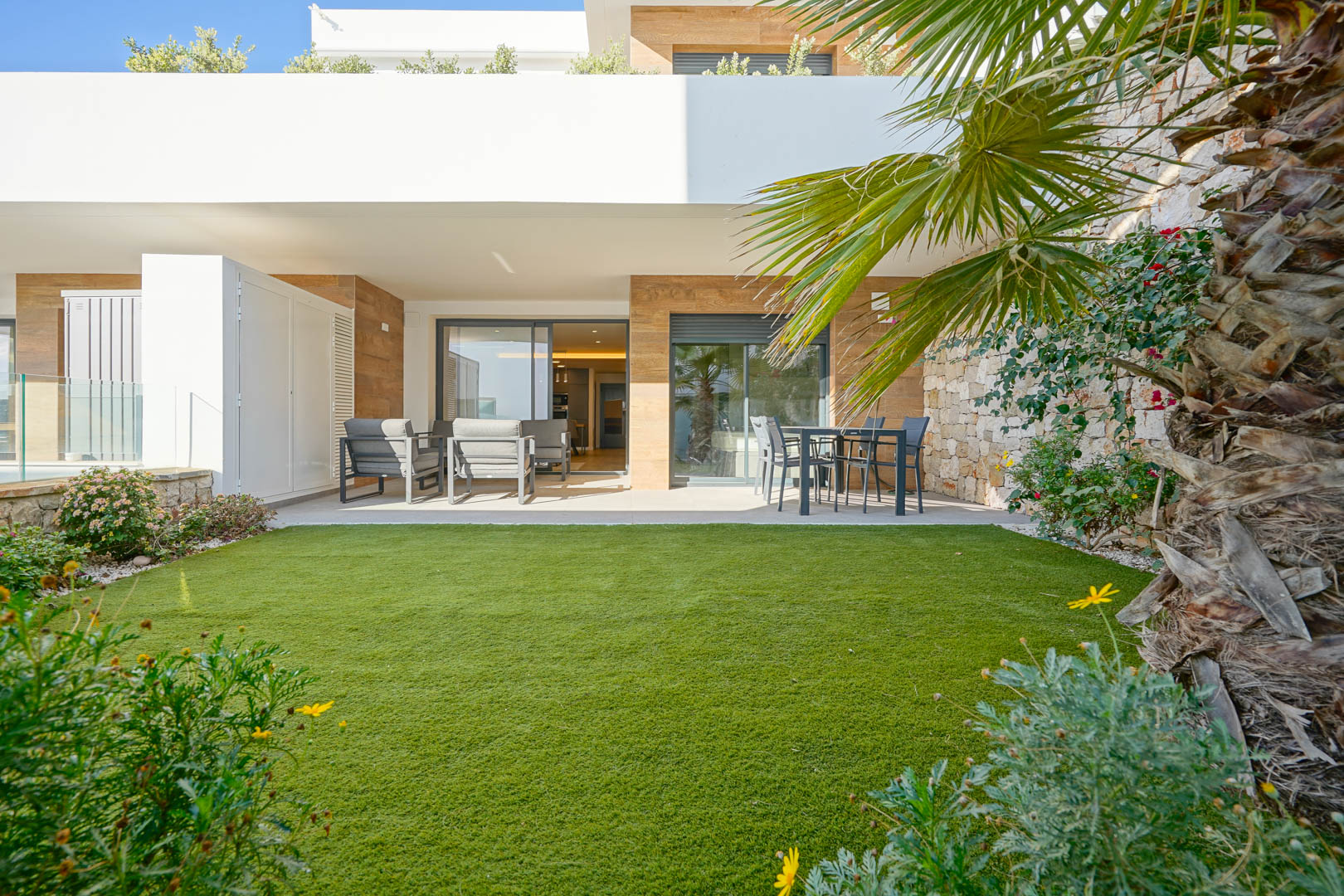 Terrasse couverte de 23 m2 et jardin privé de 36 m2 avec gazon artificiel, bordés d'un mur en pierre naturelle et offrant un accès direct à l'intérieur.