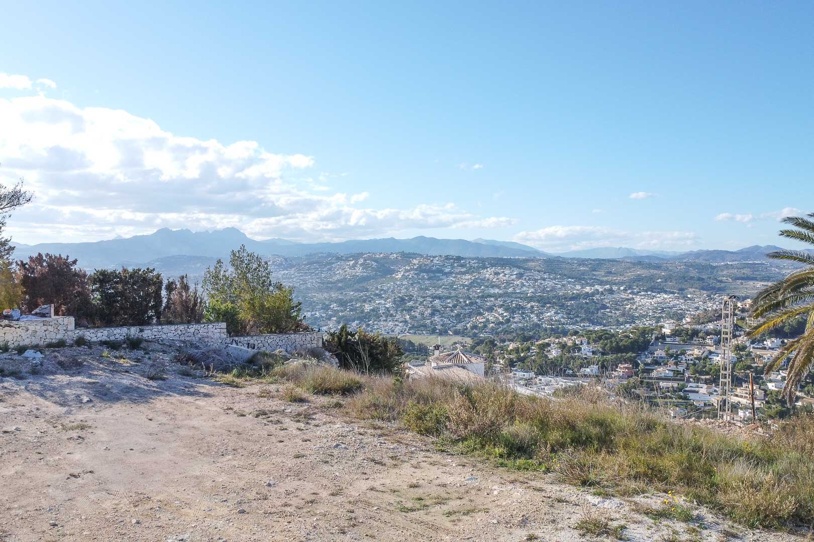 Vue panoramique de Moraira depuis un terrain surélevé avec mur en pierre et végétation.