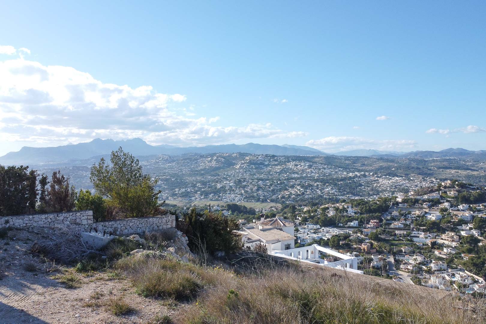 Vue panoramique de Moraira depuis une colline, mettant en valeur le paysage urbain et les montagnes au loin.