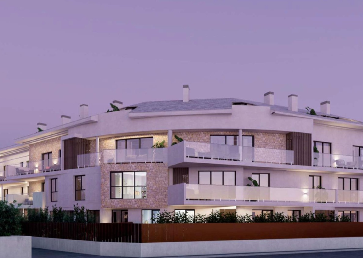 Façade extérieure du complexe résidentiel à Jávea, avec parement en pierre naturelle, grandes terrasses aux garde-corps en verre et éclairage intégré au crépuscule.