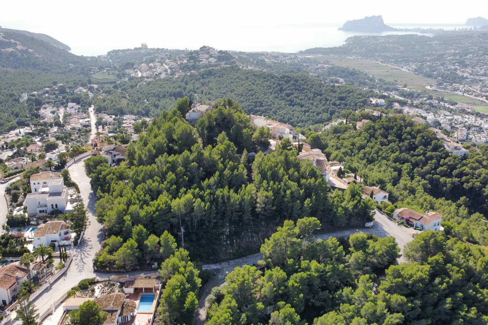 Vue aérienne de la colline boisée à Paichi, illustrant l'emplacement du terrain parmi les pins avec le Peñón de Ifach et la mer en arrière-plan.
