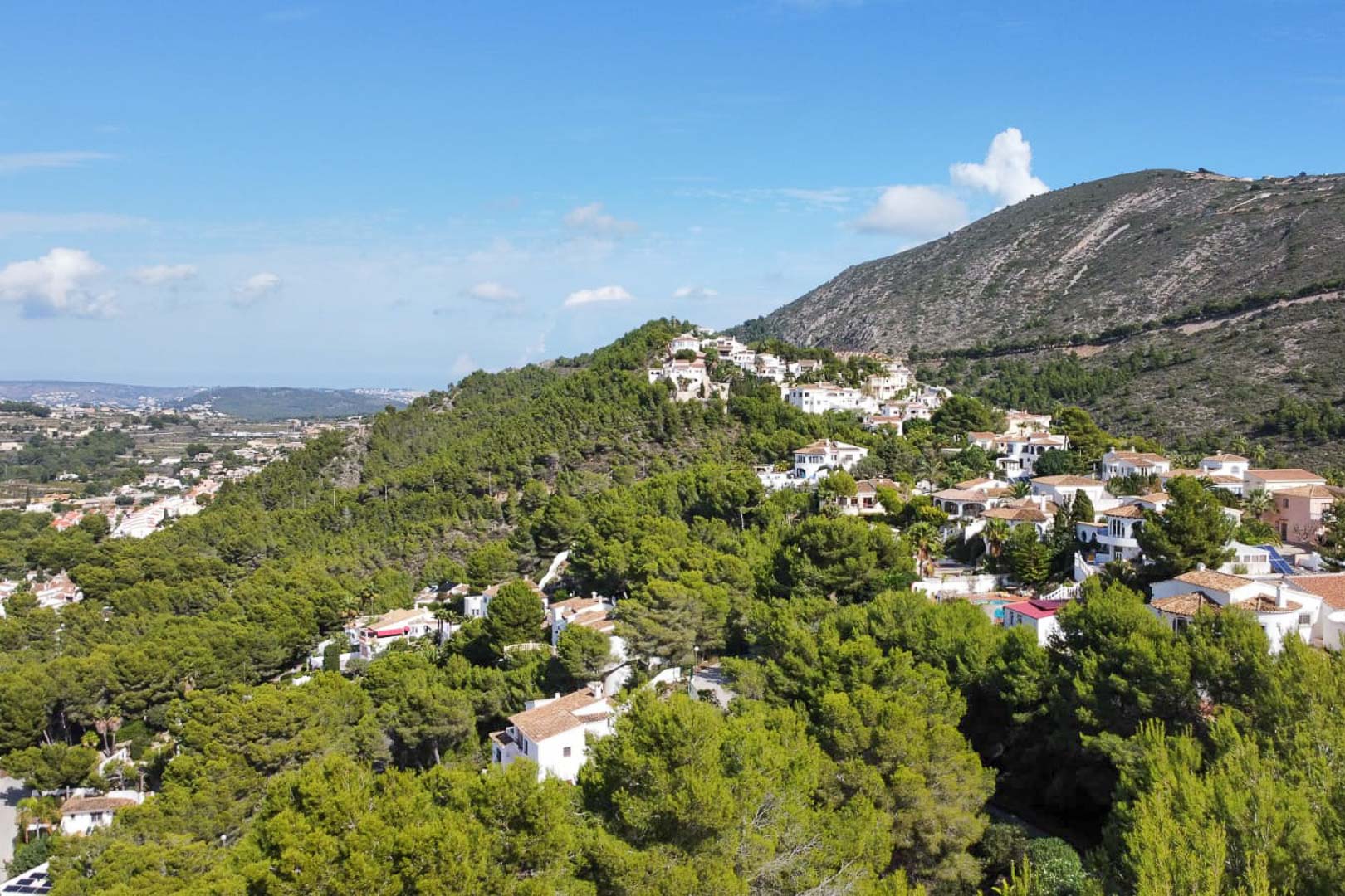 Vue aérienne du quartier résidentiel de Paichi à Moraira, illustrant l'intégration de villas blanches au cœur d'une pinède avec vue sur les montagnes.