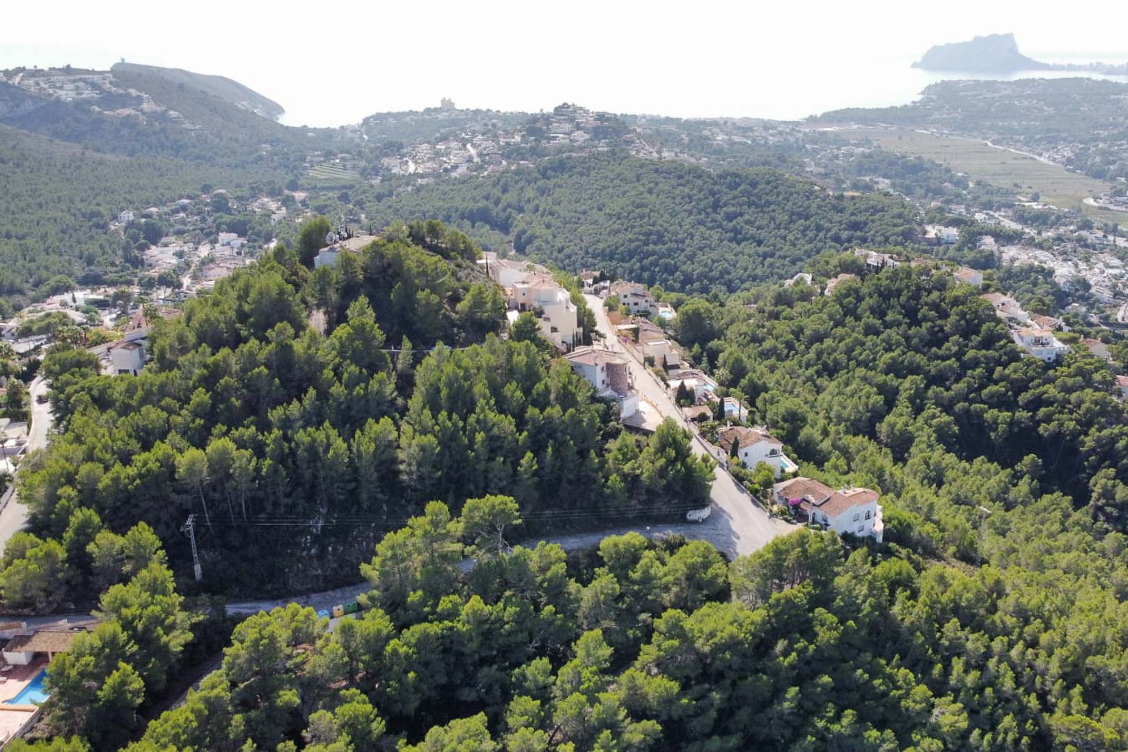 Vue aérienne du quartier résidentiel de Paichi à Moraira, montrant l'élévation du terrain boisé avec une vue dégagée sur la mer et le rocher d'Ifach.