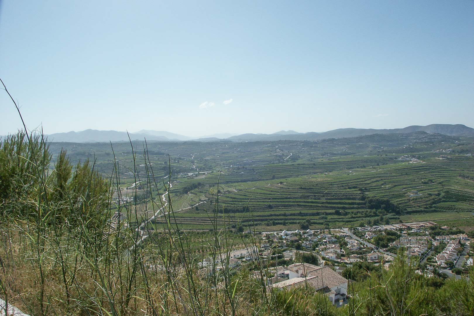 Vue panoramique depuis le terrain surélevé à Paichi, surplombant les terres agricoles en terrasses et les montagnes lointaines sous un ciel dégagé.