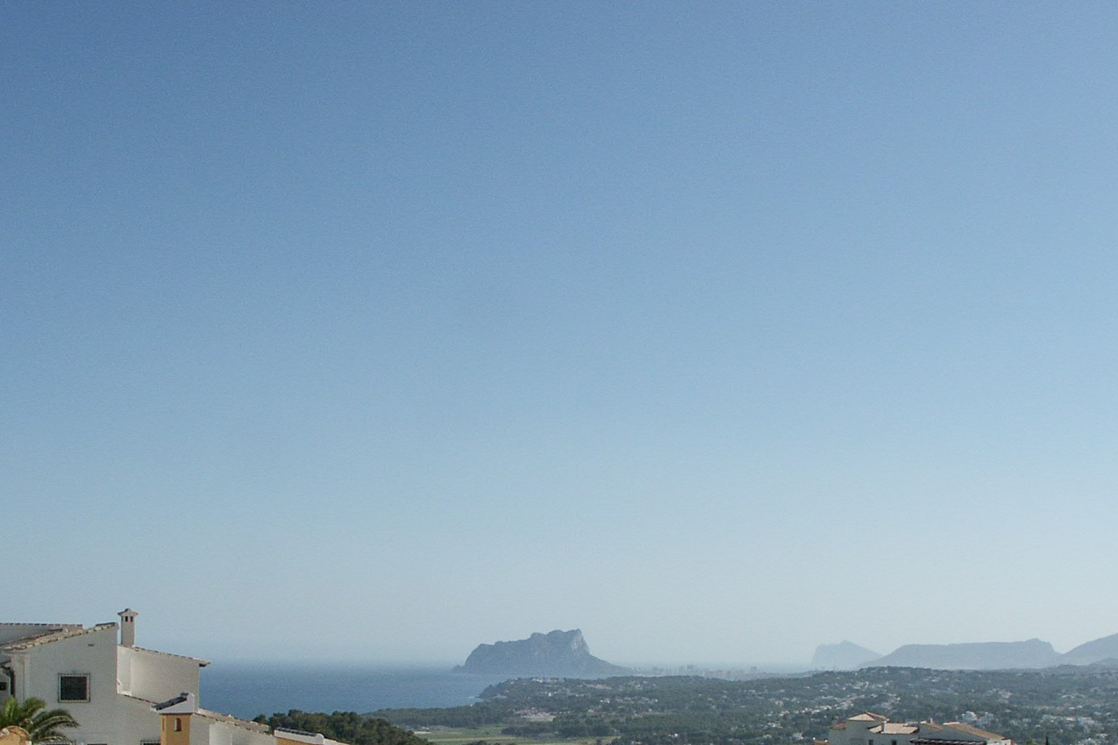 Vue panoramique depuis le terrain surélevé vers le littoral de Calpe, avec la silhouette du Peñón de Ifach se détachant sur la mer Méditerranée.