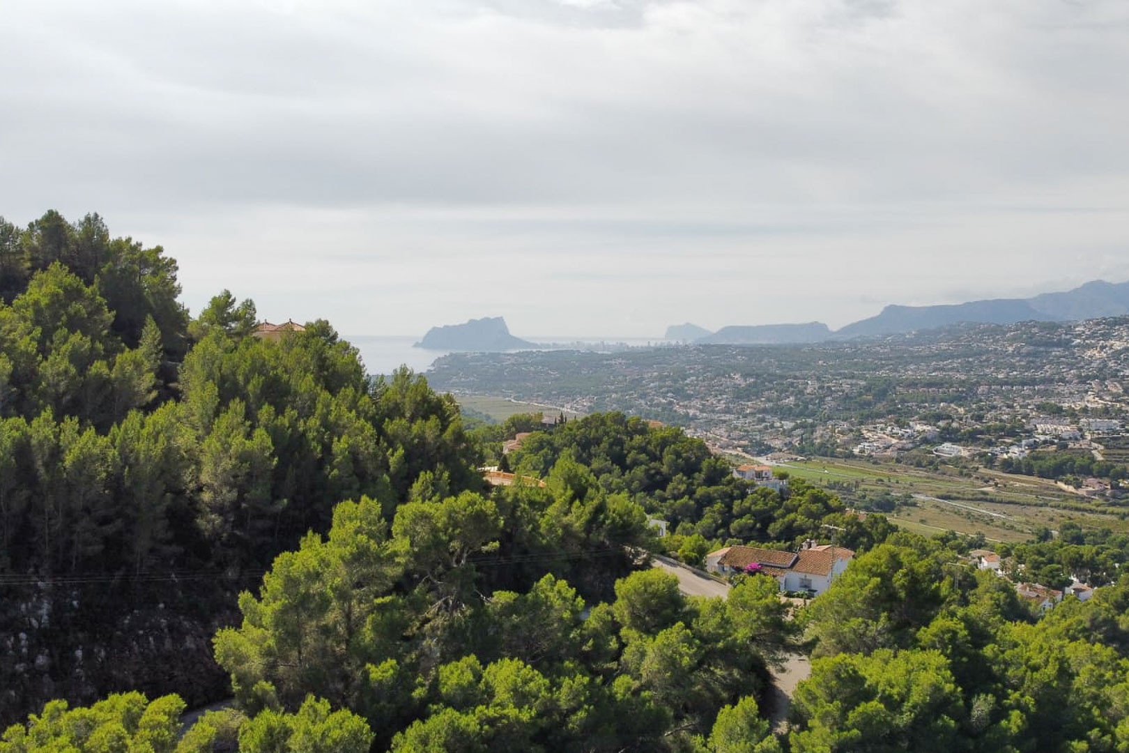 Vue panoramique surélevée depuis le terrain à Paichi, mettant en valeur la pinède, la vallée résidentielle et la silhouette du Peñón d'Ifach sur l'horizon marin.