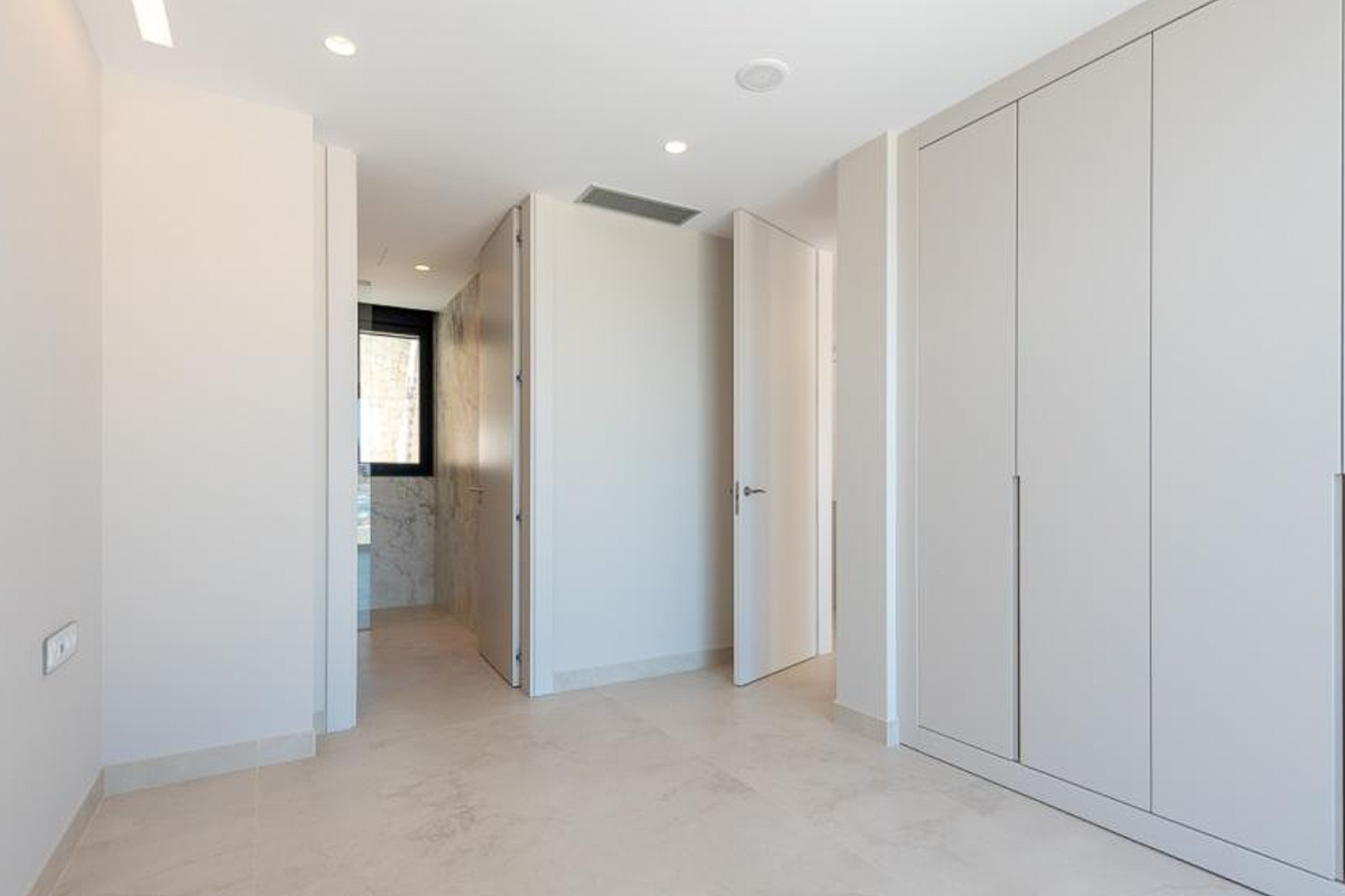 Chambre avec placards intégrés du sol au plafond, éclairage encastré et accès à une salle de bain attenante aux finitions en marbre.