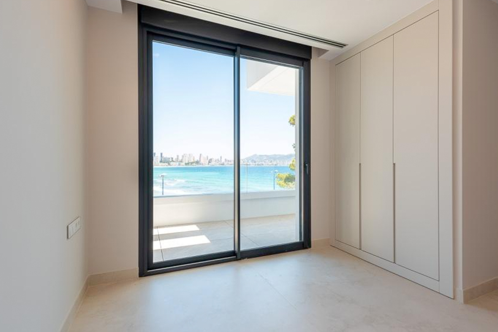 Chambre avec placards intégrés sur mesure et baie vitrée coulissante offrant une vue dégagée sur la mer et la baie de Benidorm.