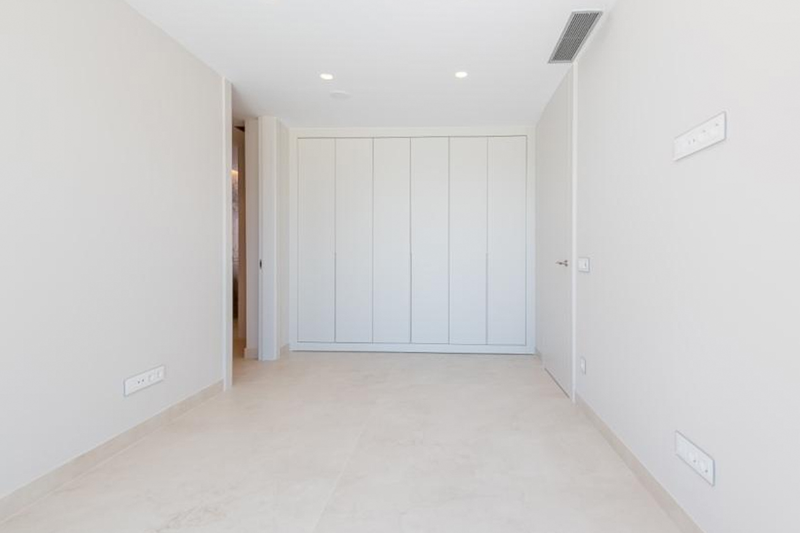 Chambre minimaliste avec de grands placards intégrés du sol au plafond, un sol en grès clair et un système de climatisation par conduits discret.