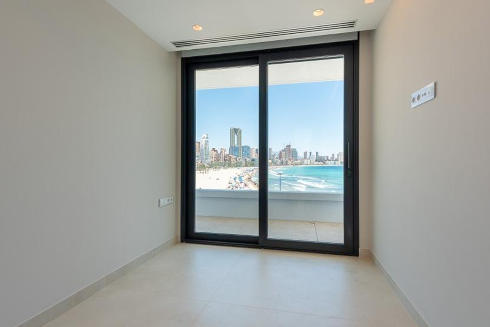 Espace lumineux avec sol en grès cérame et baie vitrée coulissante offrant une vue panoramique sur la plage et les gratte-ciels de Benidorm.