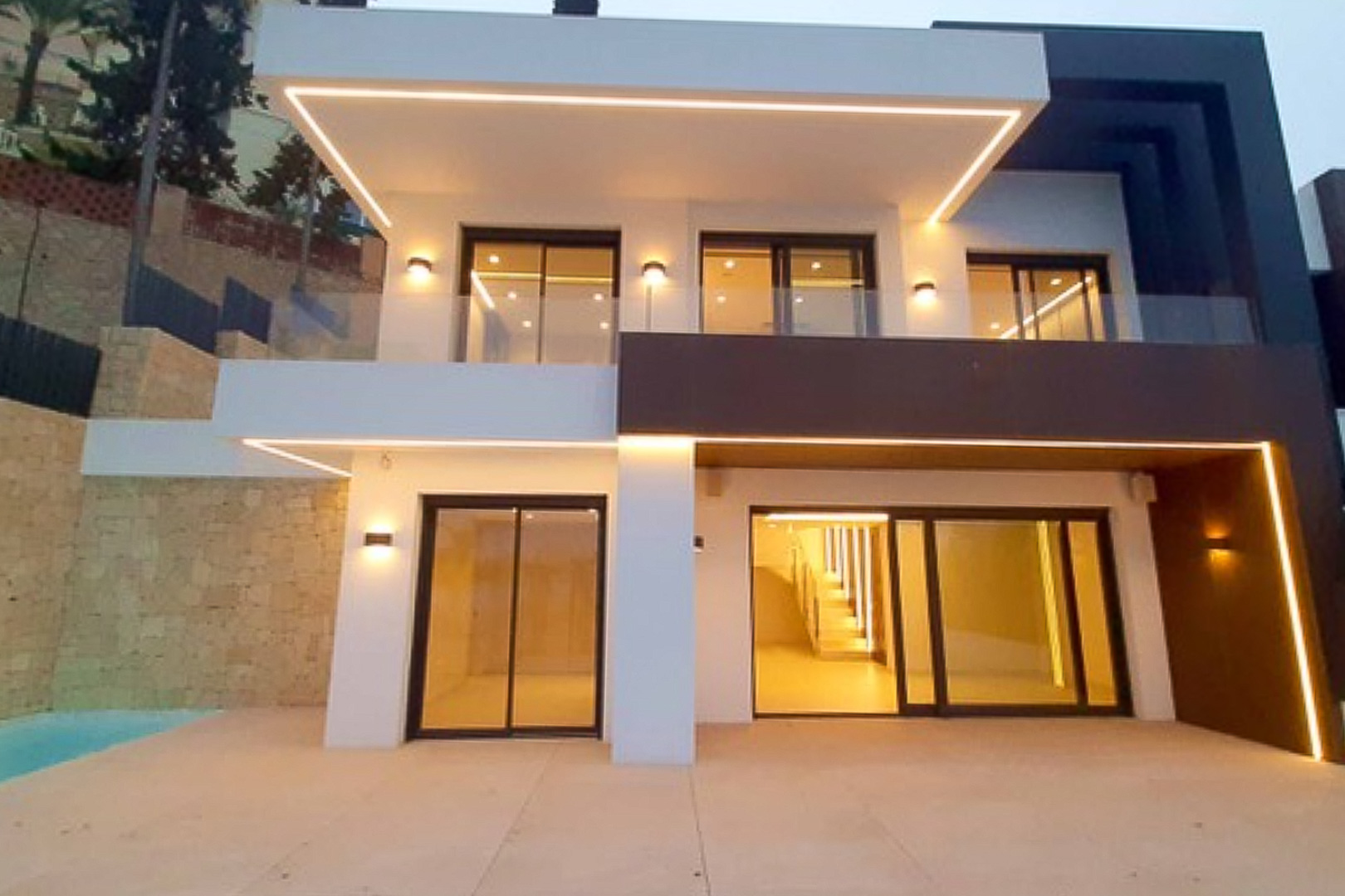 Façade moderne avec éclairage LED intégré, grandes baies vitrées coulissantes et terrasses avec garde-corps en verre aux volumes contemporains contrastés.
