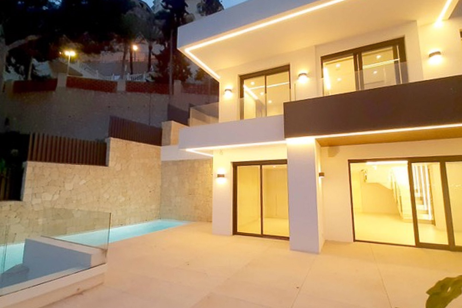 Façade moderne avec éclairage LED intégré, terrasse en grès cérame et piscine privée bordée de murs en pierre naturelle.