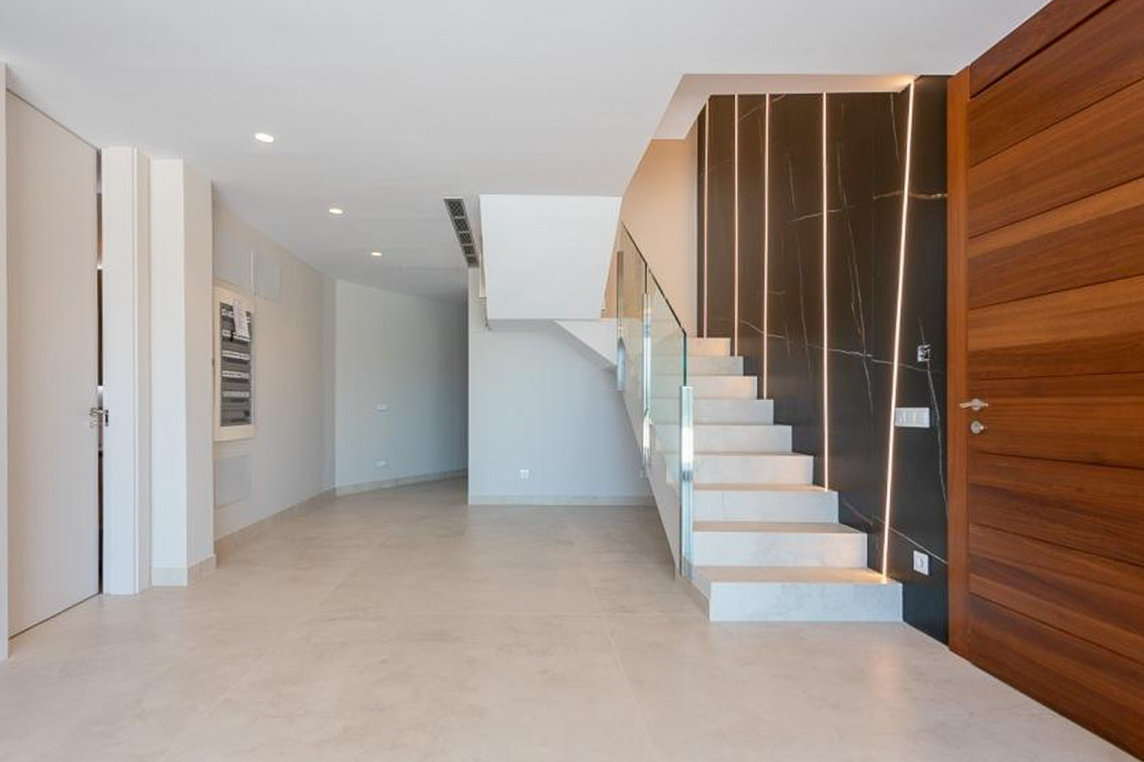 Hall d'entrée avec escalier en pierre blanche, garde-corps en verre et mur d'accent en marbre sombre doté de bandes lumineuses LED intégrées.