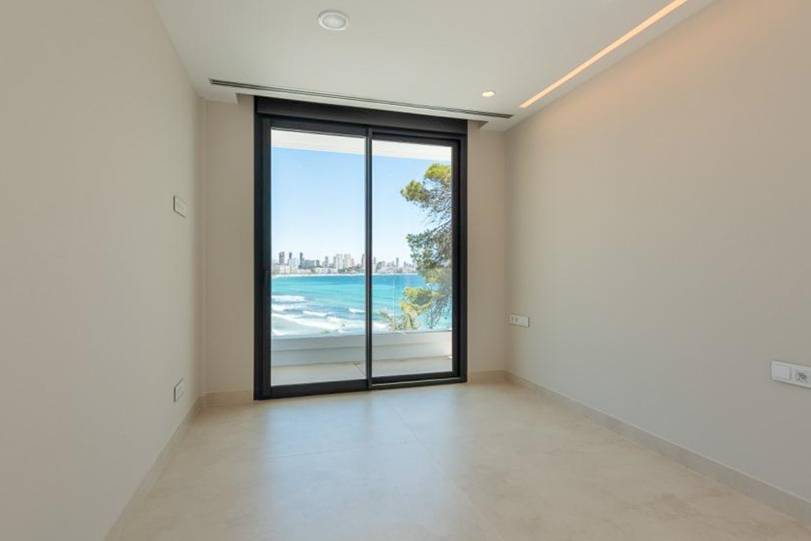 Pièce lumineuse avec sol en grès cérame, éclairage LED intégré et accès direct à une terrasse offrant une vue panoramique sur la mer et Benidorm.