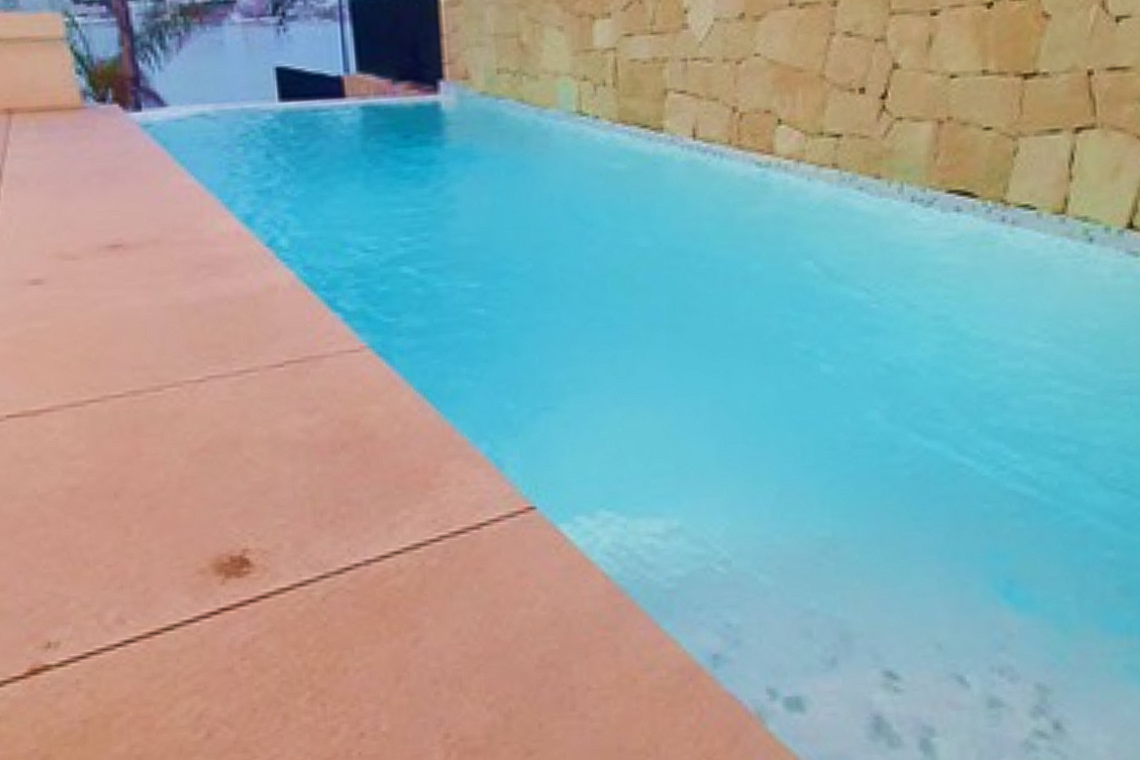 Piscine privée à débordement avec vue sur la mer, entourée d'une terrasse en grès cérame et d'un mur en pierre naturelle apparente.