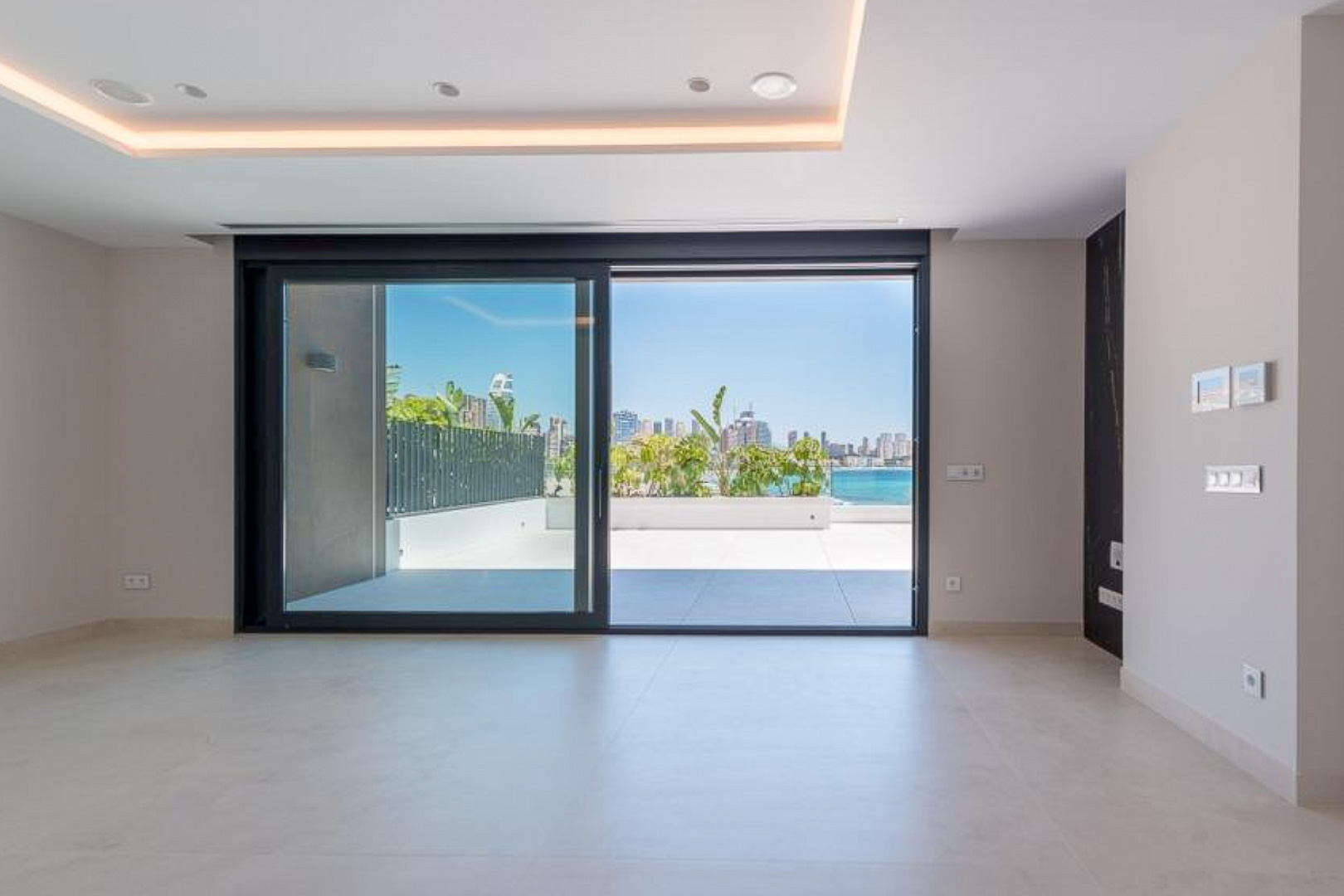 Salon lumineux avec sol en grès cérame et grandes baies vitrées coulissantes ouvrant sur une terrasse privée offrant une vue panoramique sur la baie de Benidorm.