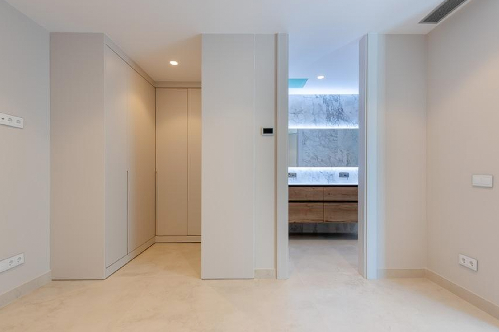 Suite parentale avec placards intégrés du sol au plafond et salle de bain attenante comprenant un revêtement en marbre, un meuble en bois et un éclairage indirect.