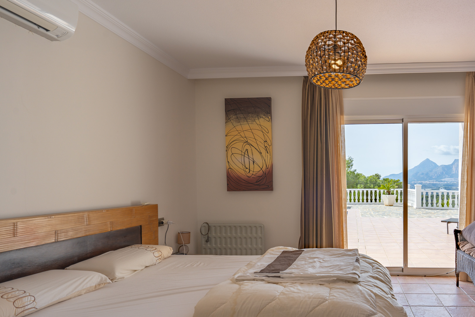 Chambre avec tête de lit en bois et climatisation, offrant un accès direct à la terrasse avec vue sur les montagnes et le Puig Campana.