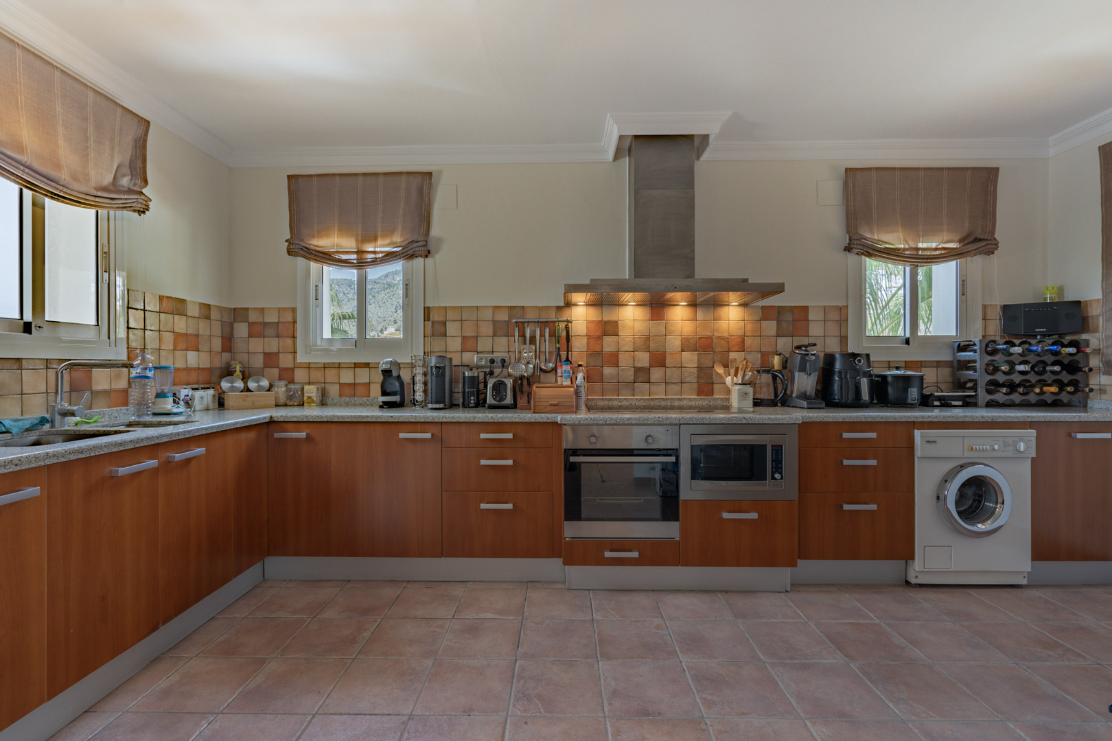 Cuisine rustique avec meubles en bois, plan de travail en granit et crédence carrelée. Elle dispose d'appareils intégrés et de fenêtres offrant une vue sur les montagnes.