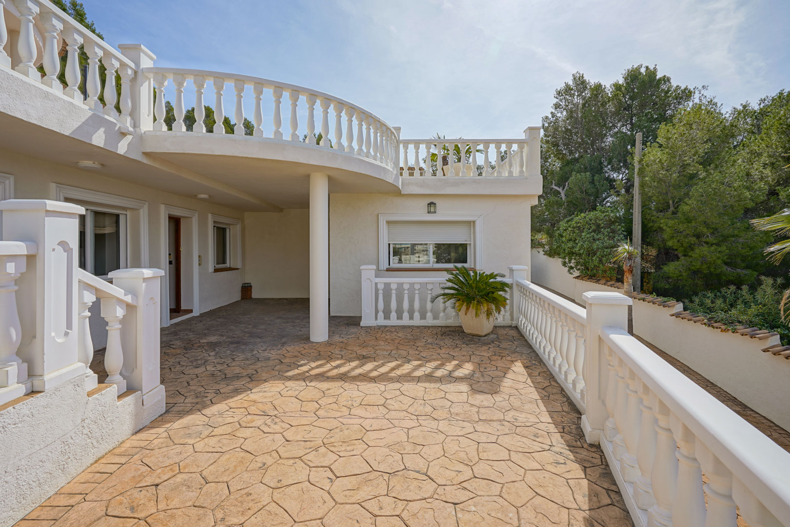 Terrasse extérieure avec revêtement en béton imprimé et balustrades blanches classiques, située sous le balcon incurvé de l'étage supérieur.