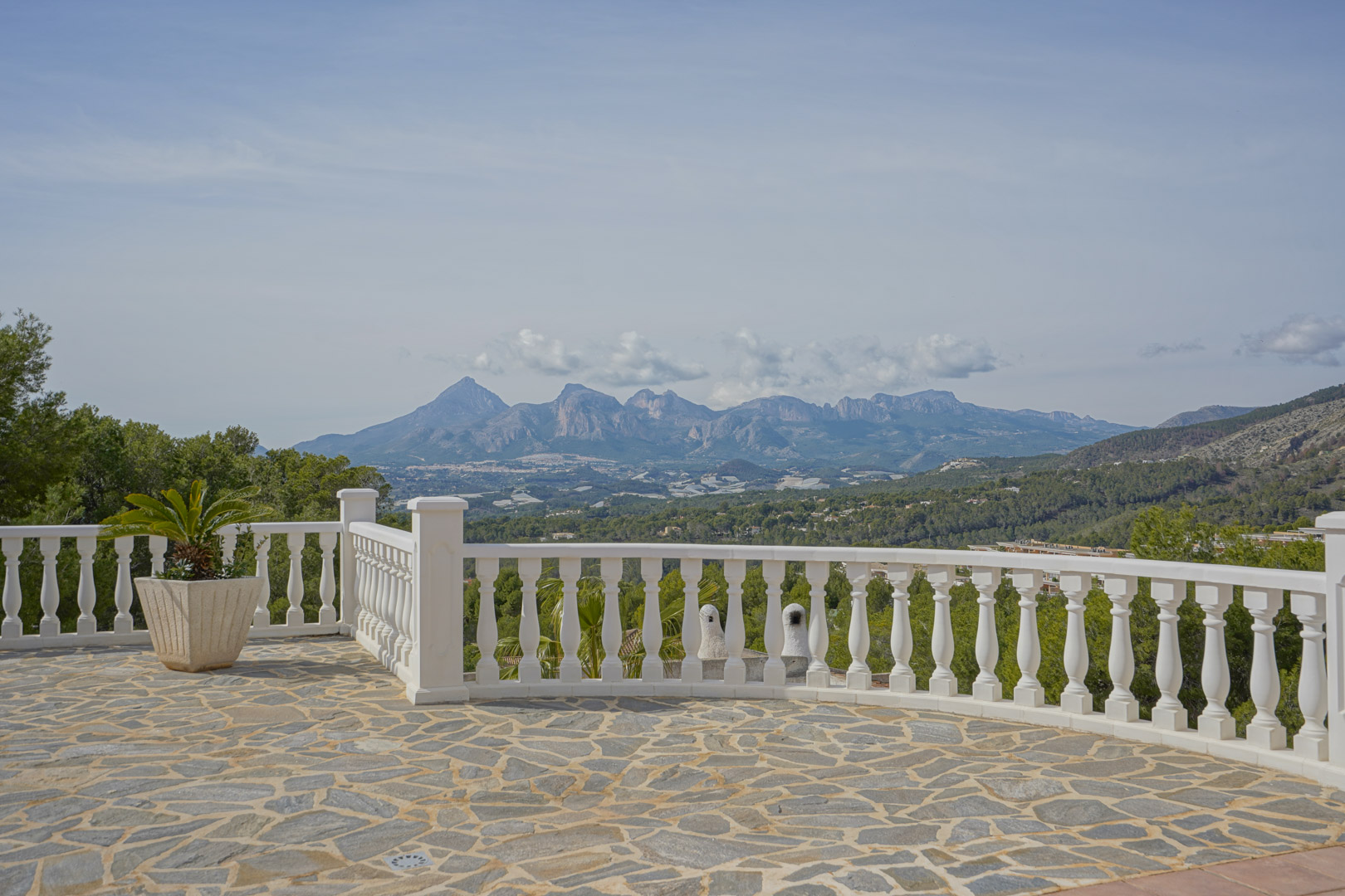 Terrasse pavée de pierres naturelles avec balustrade blanche offrant une vue panoramique sur les massifs du Puig Campana et de la Sierra Aitana.