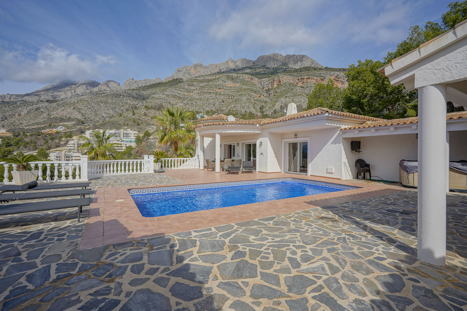 Terrasse principale avec piscine rectangulaire, bordure en mosaïque et vue sur la Sierra de Bernia. L'espace comprend un dallage en pierre naturelle, de la terre cuite et une balustrade.