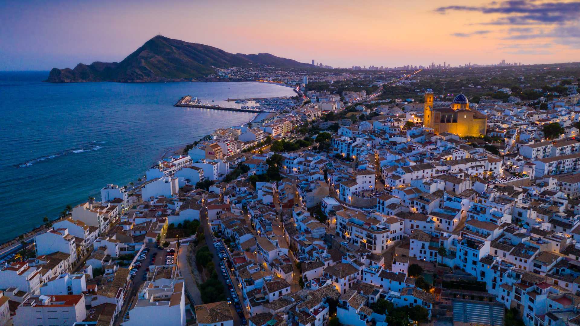 Vue aérienne d'Altea au crépuscule, mettant en valeur la vieille ville aux maisons blanches, l'église au dôme bleu emblématique et le littoral méditerranéen.