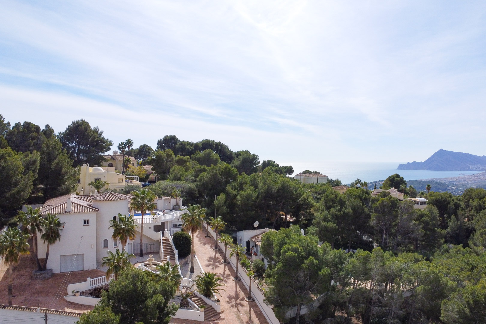 Vue aérienne de la villa méditerranéenne aux façades blanches, entourée d'une pinède dense et offrant un panorama sur la mer et le littoral d'Altea.