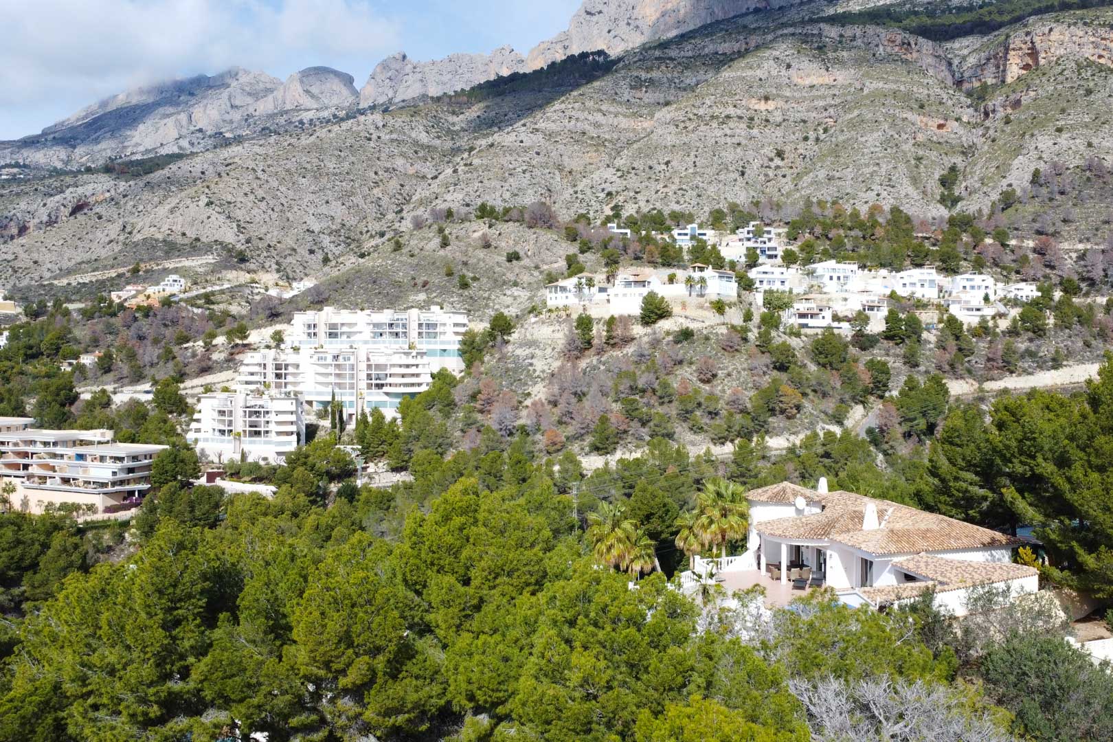 Vue aérienne de la villa méditerranéenne aux toits de tuiles, entourée de pins au pied de la chaîne de montagnes Sierra de Bernia à Altea.