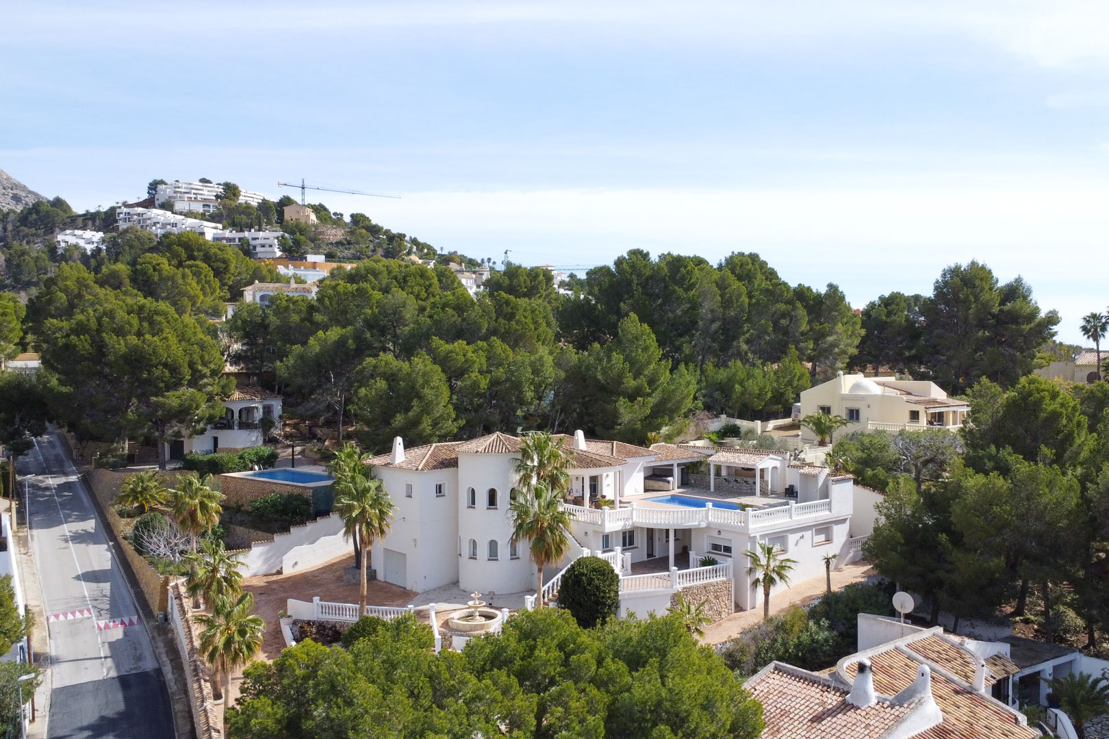 Vue aérienne de la villa méditerranéenne avec sa façade blanche, sa tour circulaire et sa terrasse avec piscine entourée d'une pinède luxuriante à Altea.