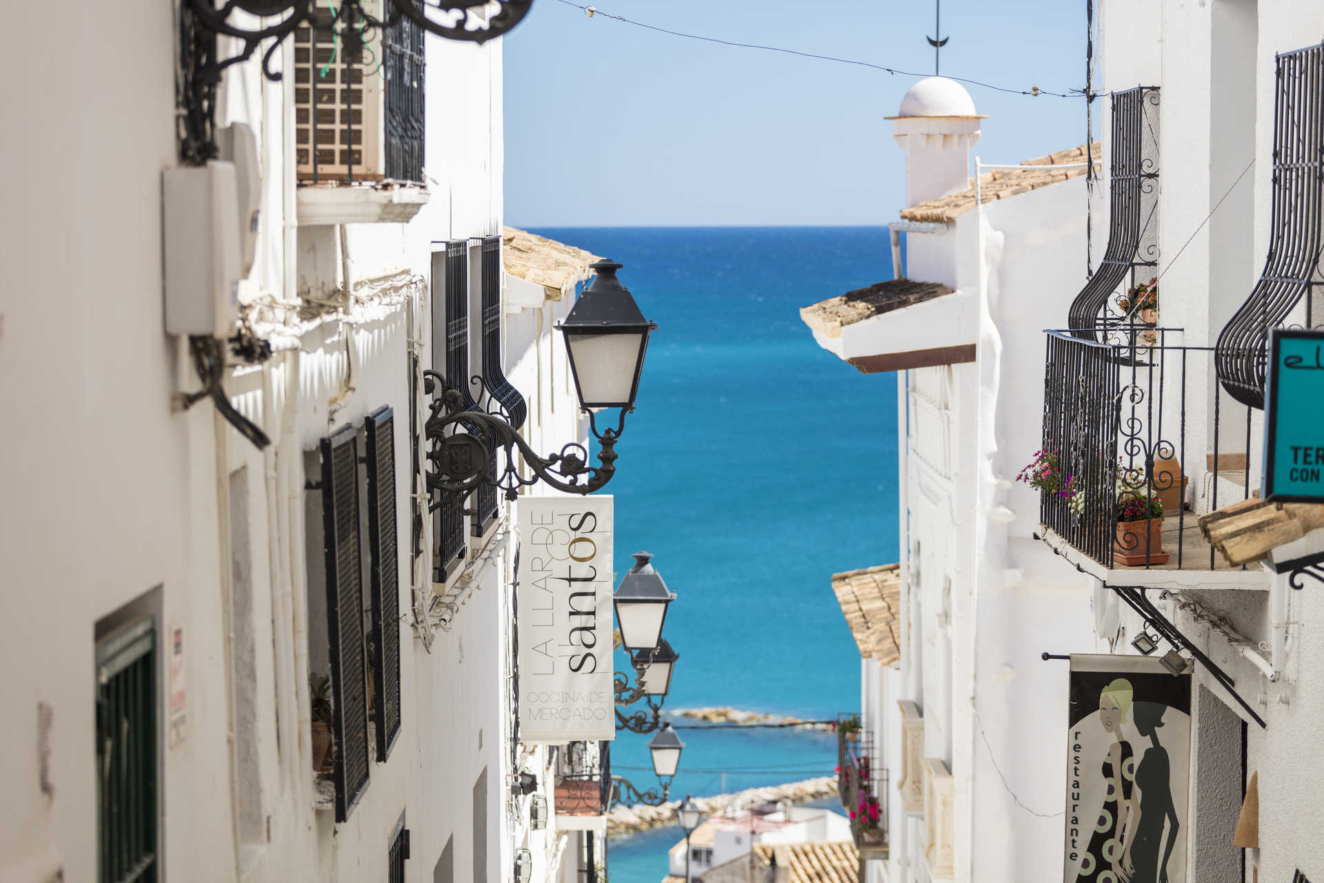 Vue d'une ruelle étroite de la vieille ville d'Altea, avec ses façades blanches, ses lanternes en fer forgé et une vue imprenable sur la mer Méditerranée.