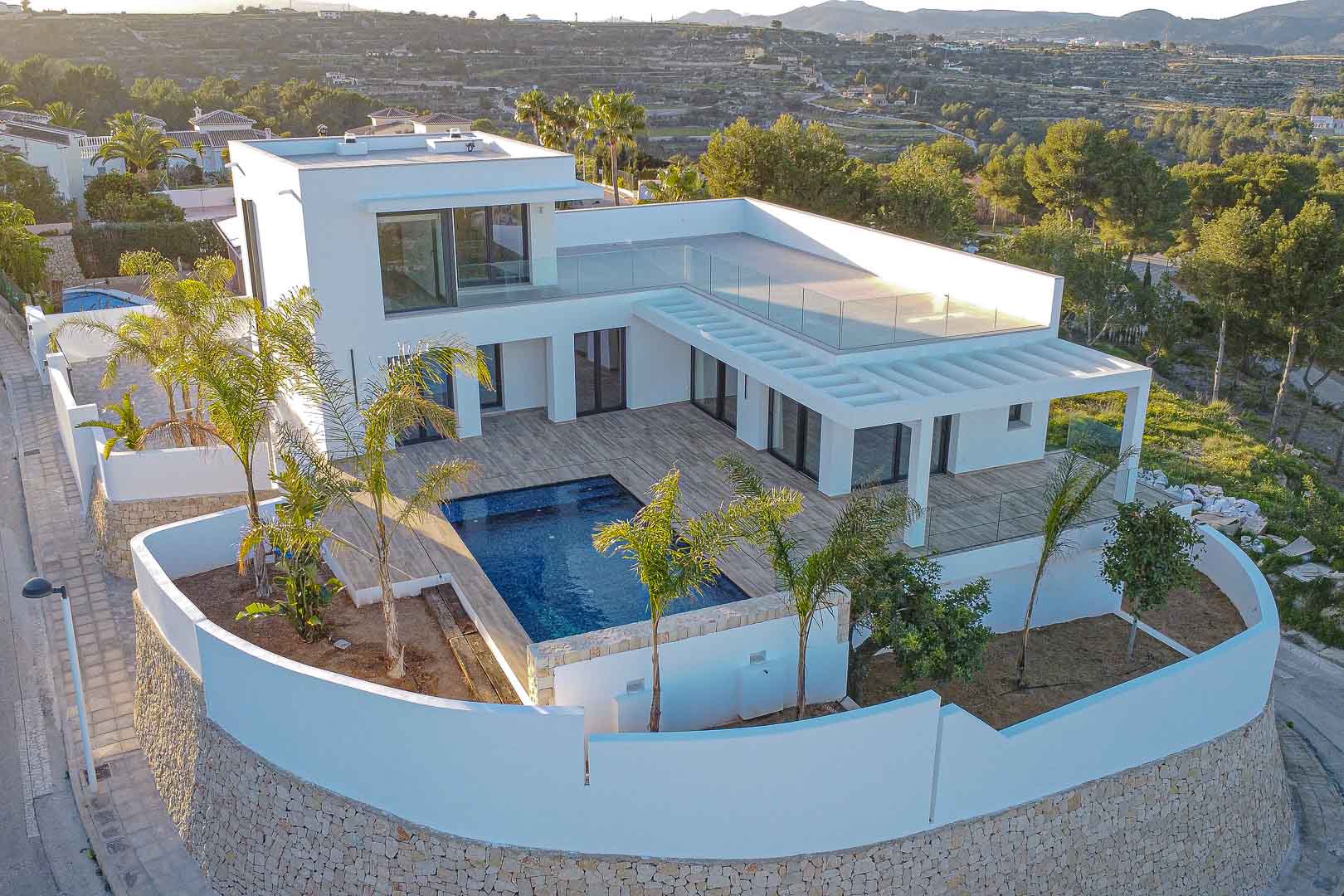 Vue aérienne d'une villa moderne avec piscine bleue et murs blancs avec détails en pierre à Benimeit, Moraira.