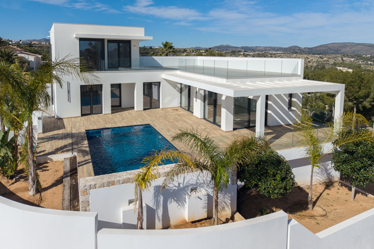 Vue aérienne d'une villa moderne avec piscine bleue, terrasse en bois et garde-corps en verre à Benimeit, Moraira.