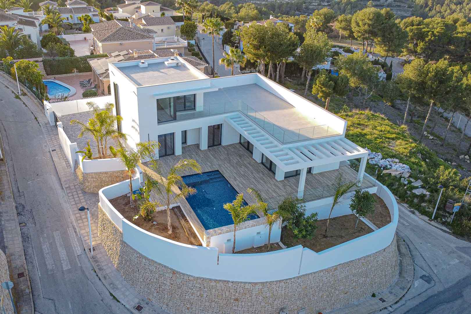 Vue aérienne d'une villa moderne avec piscine bleue, terrasse en bois et jardin méditerranéen à Benimeit, Moraira.