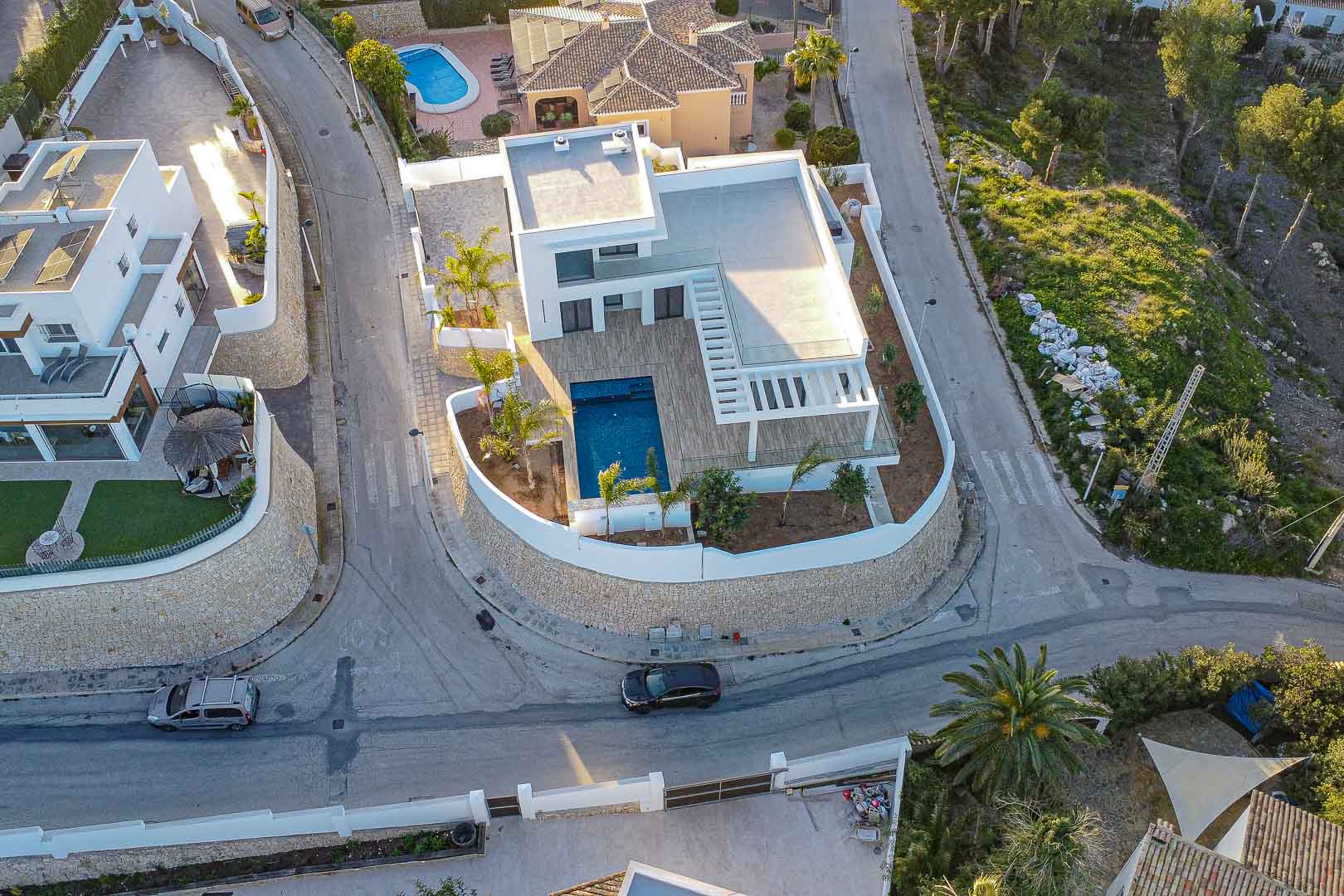 Vue aérienne d'une villa moderne avec piscine bleue, terrasses en bois et jardin méditerranéen à Benimeit, Moraira.