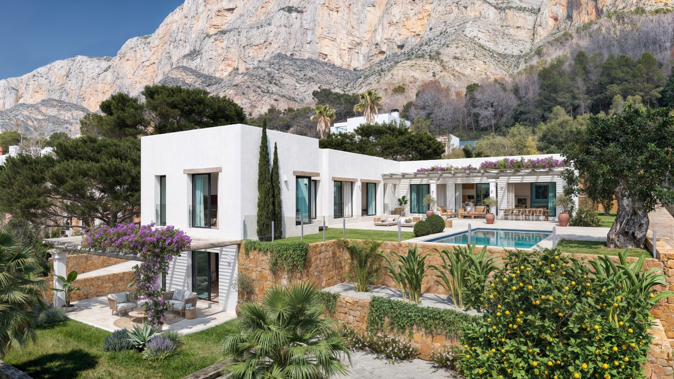 Vue extérieure de la villa avec façades blanches, piscine privée et murs en pierre naturelle, nichée au pied des falaises spectaculaires du Montgó.