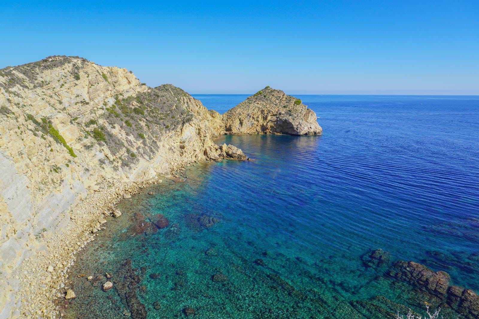 Vue panoramique du littoral de Jávea avec des falaises escarpées et des eaux turquoise cristallines bordant la côte rocheuse.