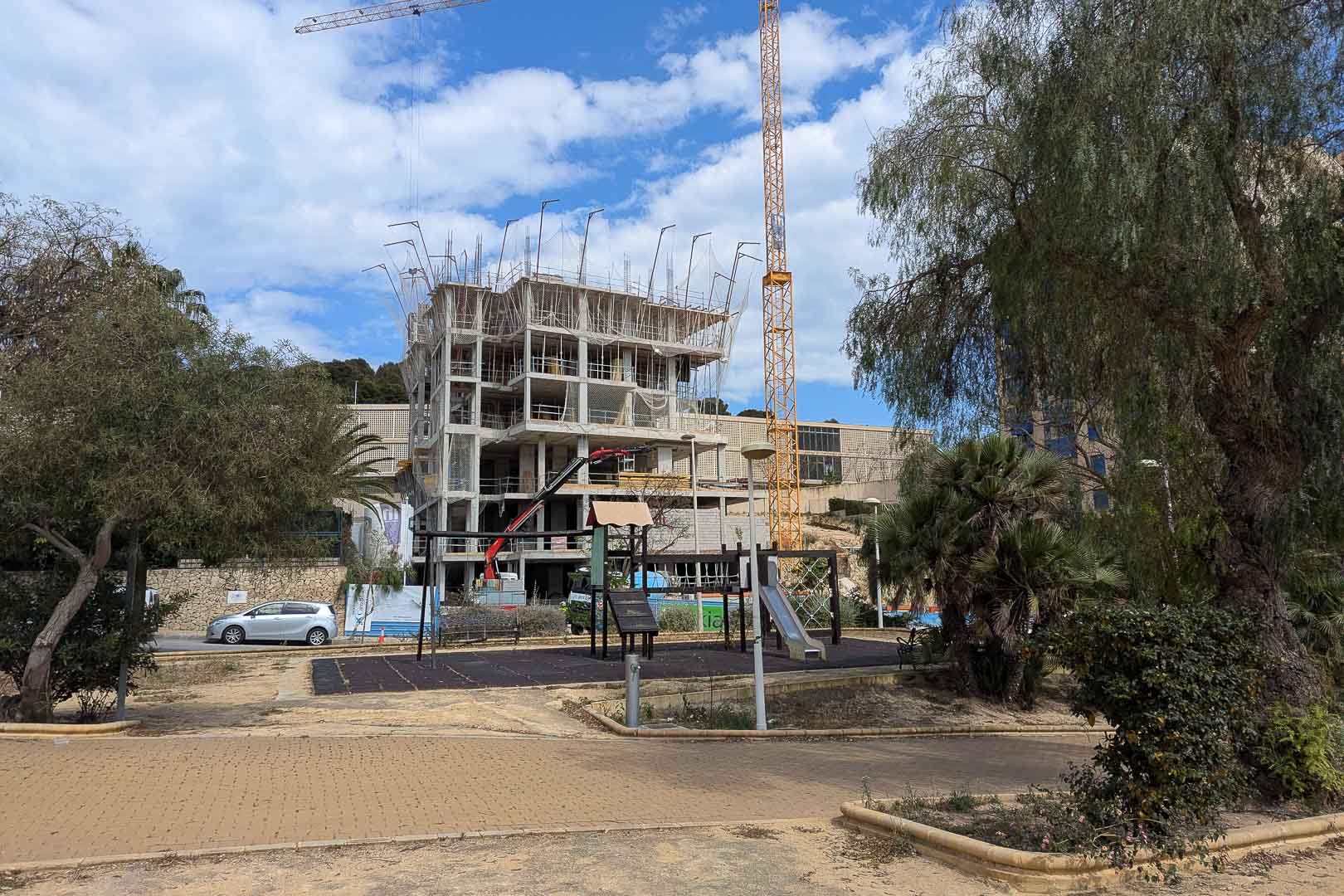 État d'avancement des travaux à Calpe, montrant la structure en béton armé du bâtiment et les grues de chantier à proximité d'un parc de jeux.