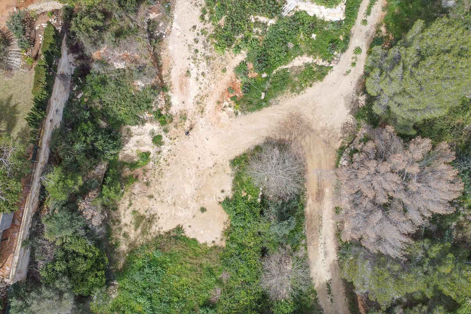 Vue aérienne du terrain à bâtir dans l'urbanisation La Corona, illustrant le sol naturel et la végétation environnante avant le début des travaux de construction.
