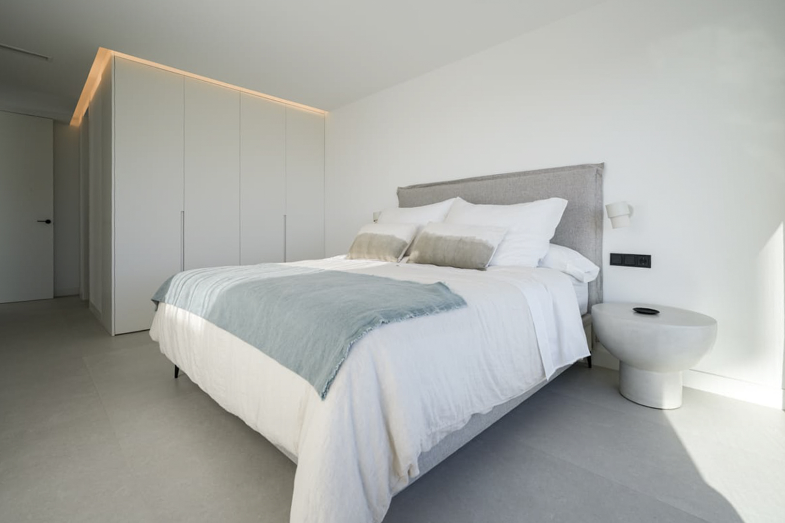 Chambre lumineuse avec lit double, linge de maison blanc et armoire encastrée avec éclairage supérieur.