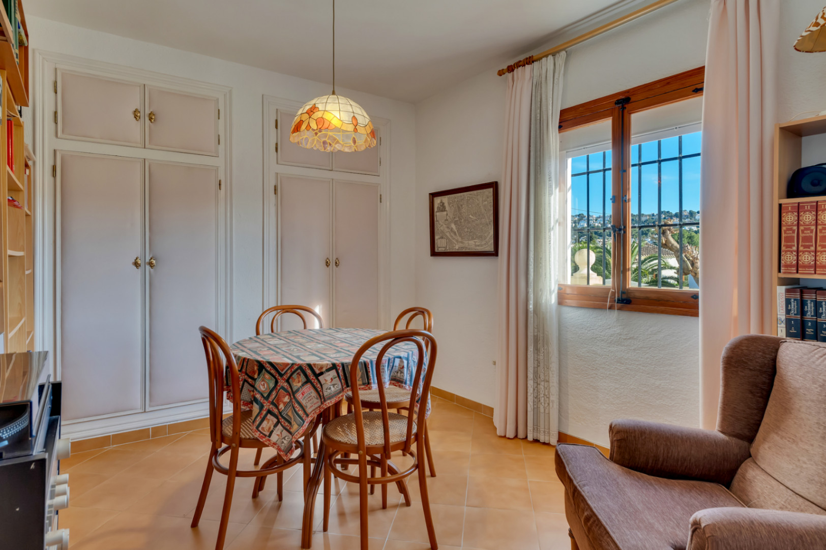 Espace repas lumineux avec placards intégrés blancs, table ronde et chaises en bois. La fenêtre à cadre en bois apporte une lumière naturelle et offre une vue sur le quartier.
