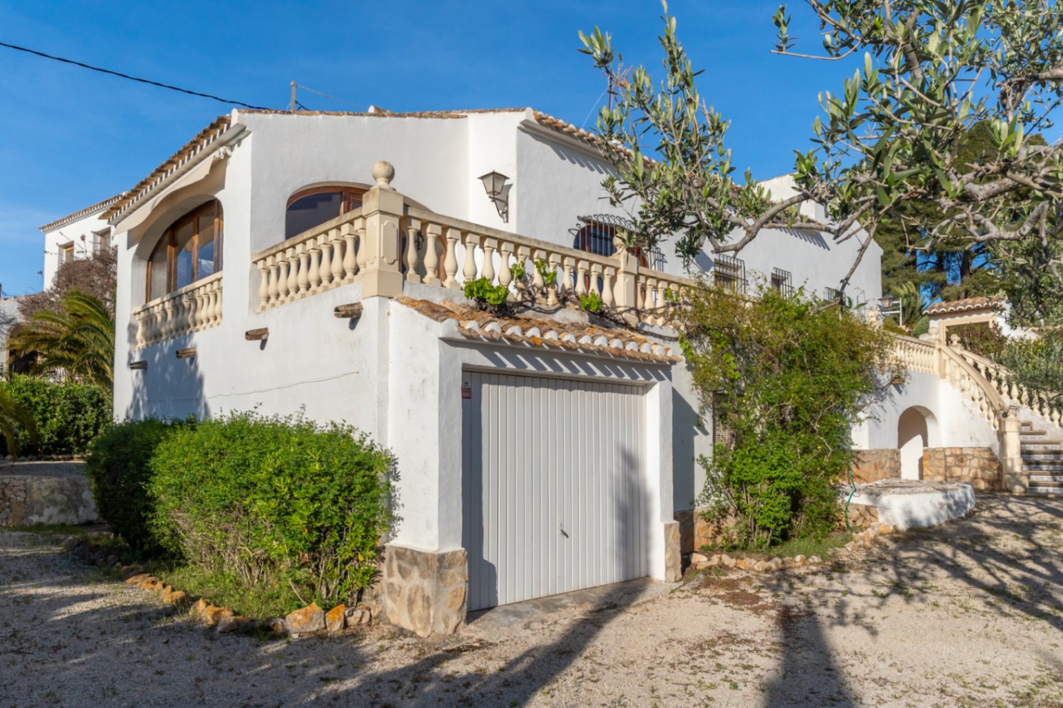 Façade de villa méditerranéenne avec garage privé, terrasse à balustrade en pierre et architecture traditionnelle blanchie à la chaux à Jávea.