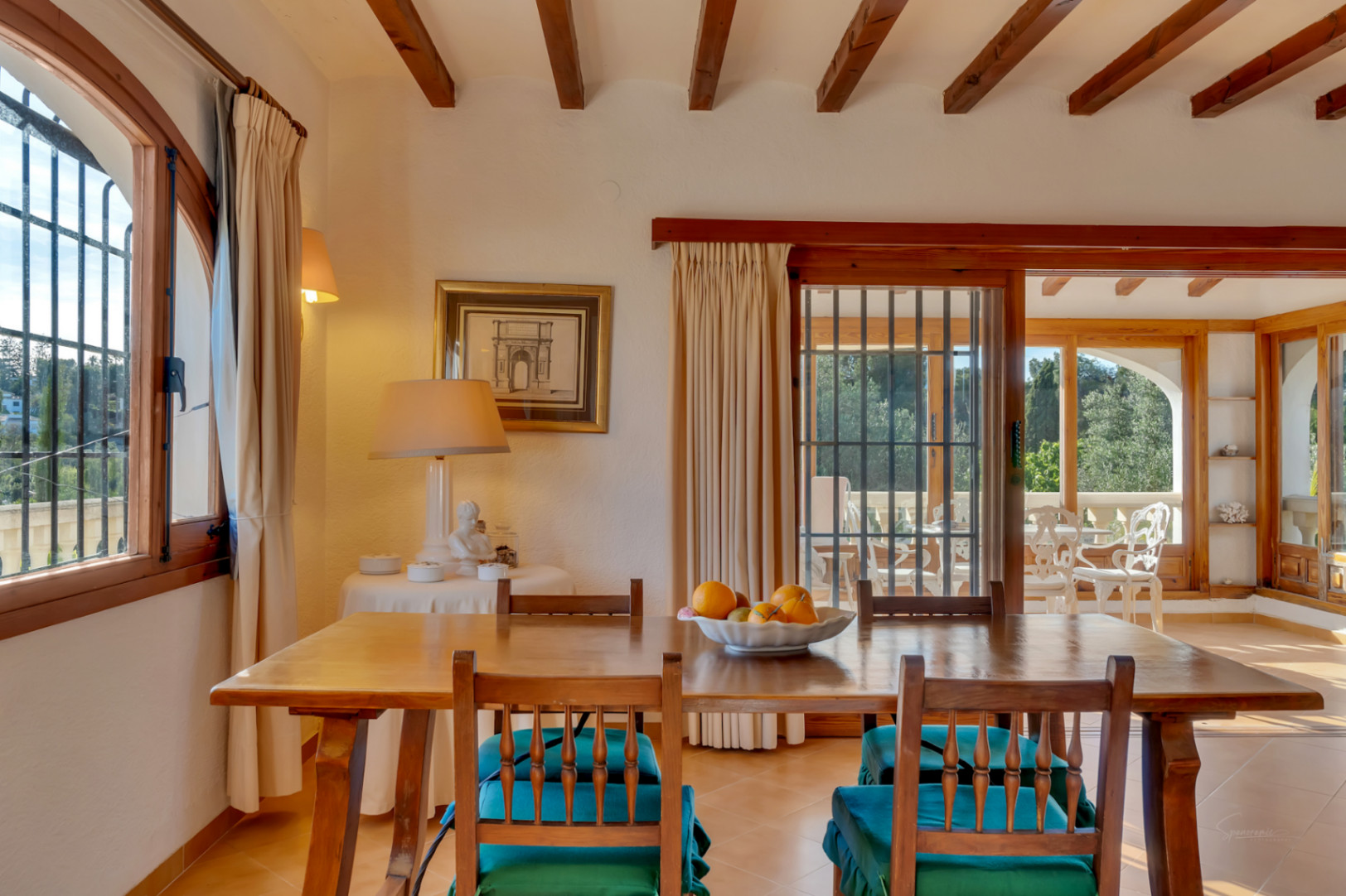 Salle à manger avec poutres apparentes, mobilier en bois et accès à la terrasse vitrée par des portes coulissantes offrant une belle luminosité.