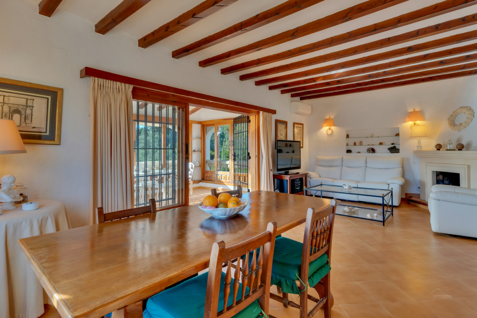 Salon-salle à manger lumineux avec poutres en bois apparentes, sol en terre cuite et accès direct à la terrasse vitrée par de grandes baies vitrées.