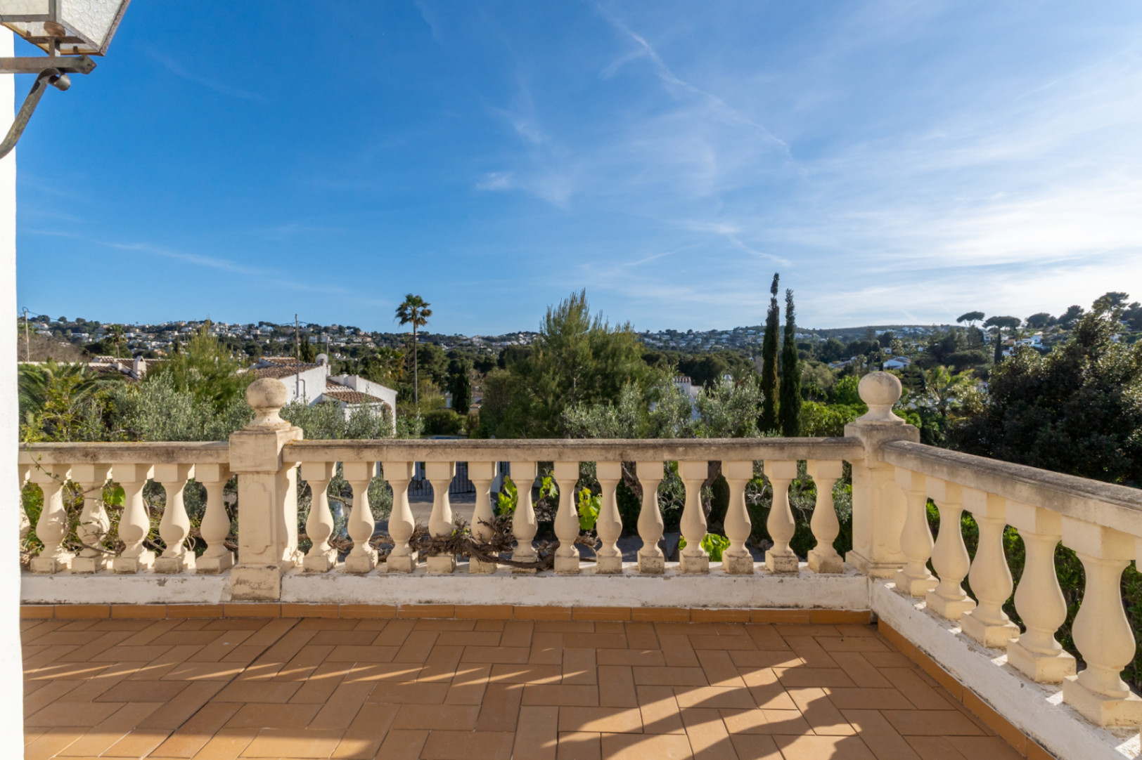 Terrasse surélevée avec sol en terre cuite et balustrade classique en pierre, offrant une vue dégagée sur le quartier résidentiel et la végétation de Jávea.